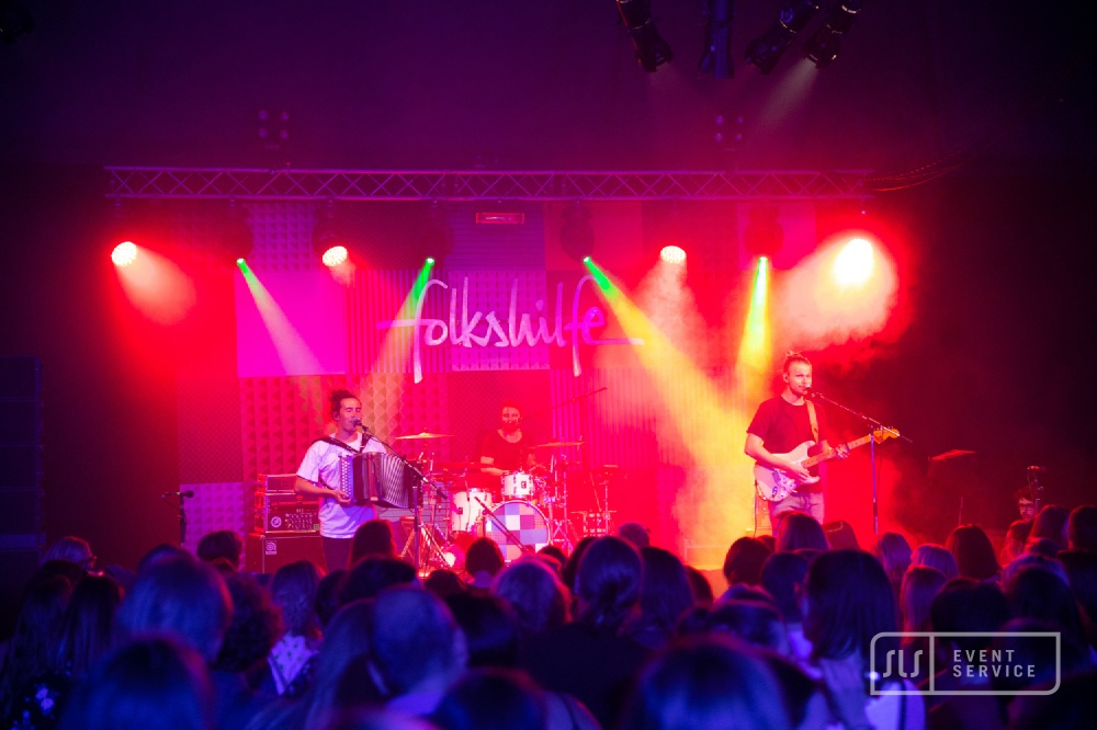 Live-Konzert der Band Folkshilfe mit Akkordeon, Schlagzeug und Gitarre vor großem Publikum