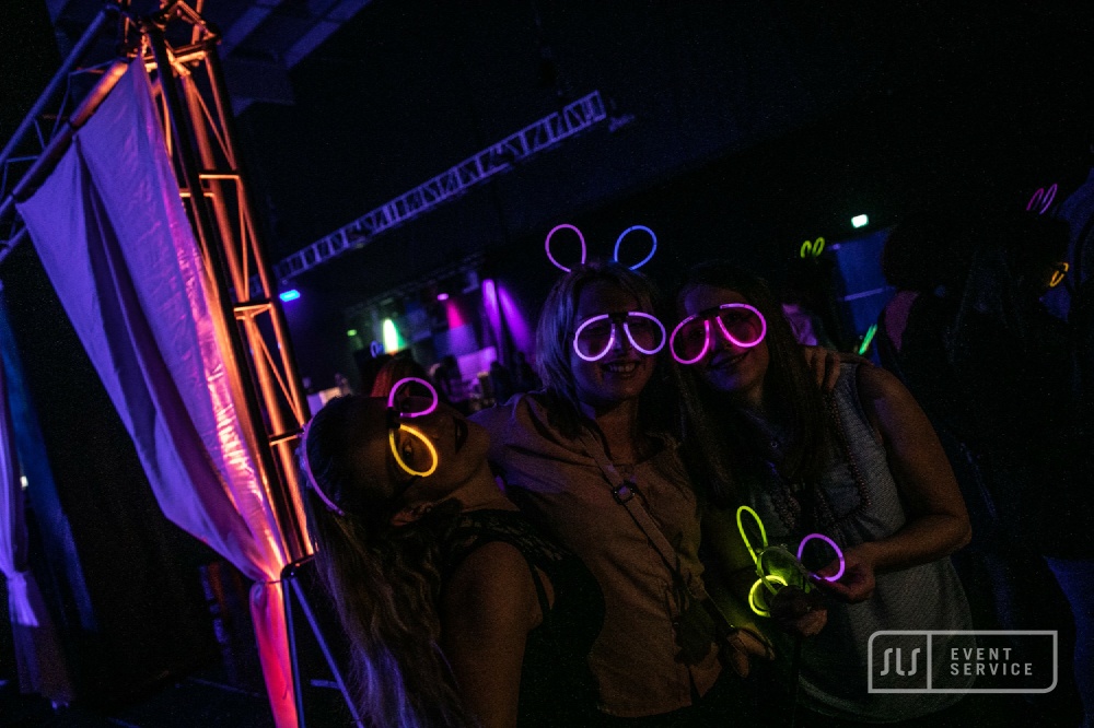 Drei Gäste bei einer Party mit leuchtenden Neonbrillen und Knicklichtern
