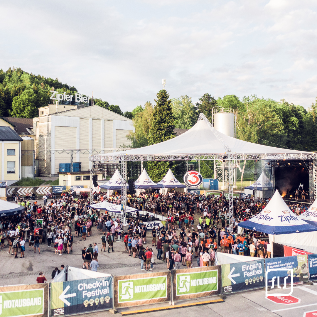 Erhöhte Ansicht des ZipfAir-Festivalgeländes mit Publikum, Zipfer-Zelten und großer Main Stage