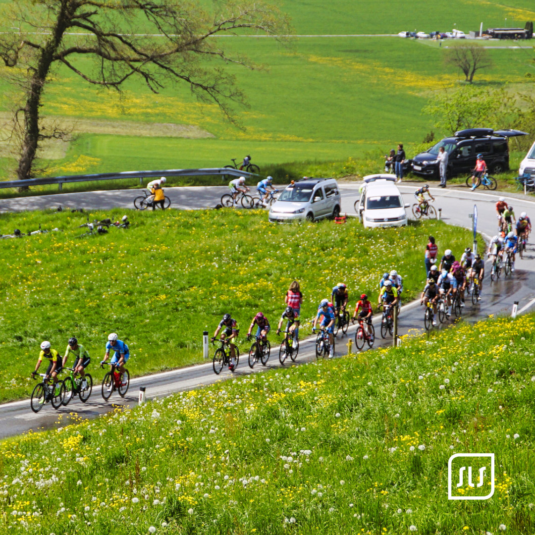 Langgezogenes Feld von Rennradfahrern fährt beim 12. GP Vorarlberg durch eine grüne Wiesenlandschaft