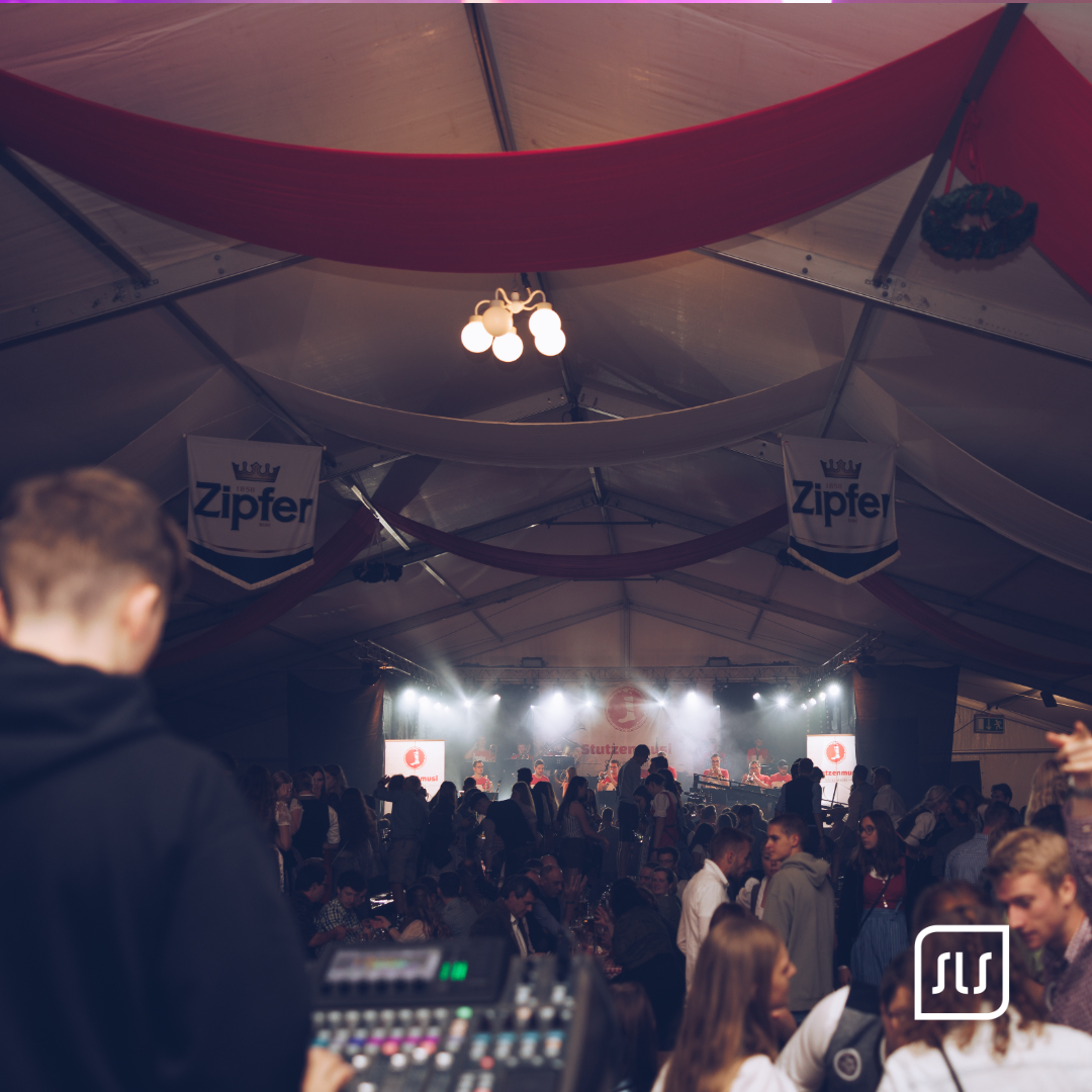 Blick über ein Mischpult und Gäste auf die beleuchtete Bühne im Festzelt des Schiedlberger Oktoberfests