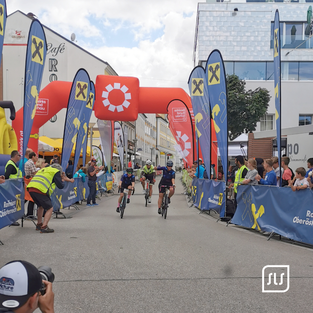 Drei Radfahrer fahren zwischen Publikum und Werbefahnen ins Ziel des 24-Stunden-Radmarathons in Grieskirchen