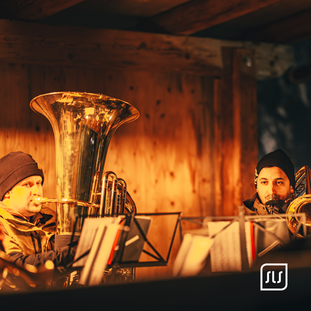 Zwei Musiker spielen Tuba und Posaune im warm beleuchteten Holzstand beim Adventzauber in St. Anton