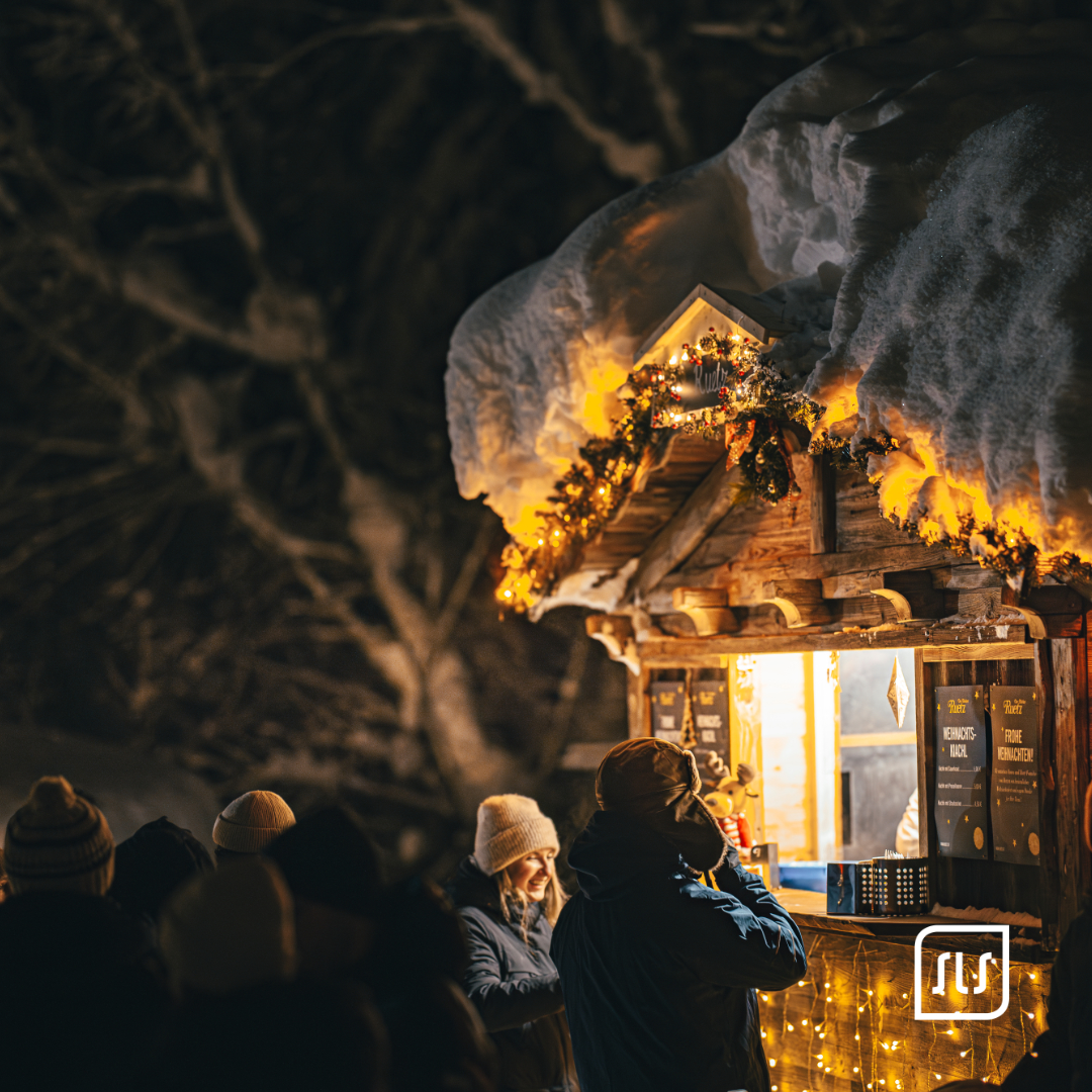Beleuchteter Holzstand mit Tannengirlanden und schneebedecktem Dach beim Adventzauber in St. Anton