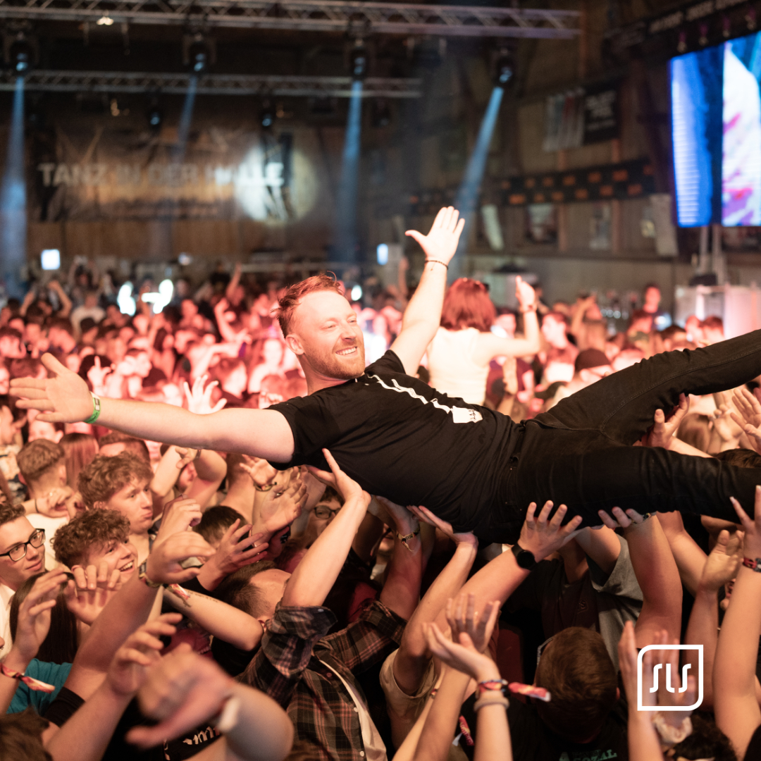 Mann mit ausgebreiteten Armen wird beim Crowdsurfing von Konzertgästen über den Köpfen getragen
