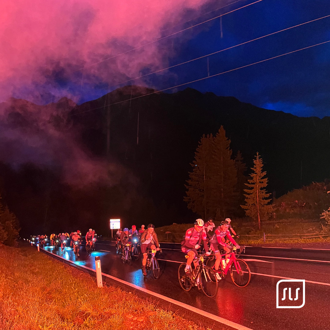 Gruppe von Radfahrern fährt beim Arlberg Giro 2023 in der Dämmerung auf einer nassen Bergstraße