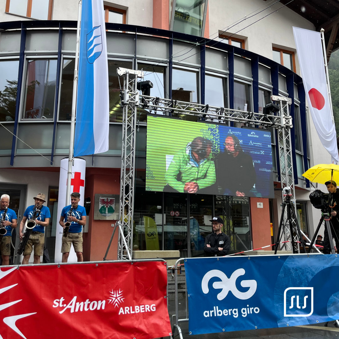 LED-Wall zeigt ein Interview beim Arlberg Giro vor Fahnen und Veranstaltungsbannern in St. Anton