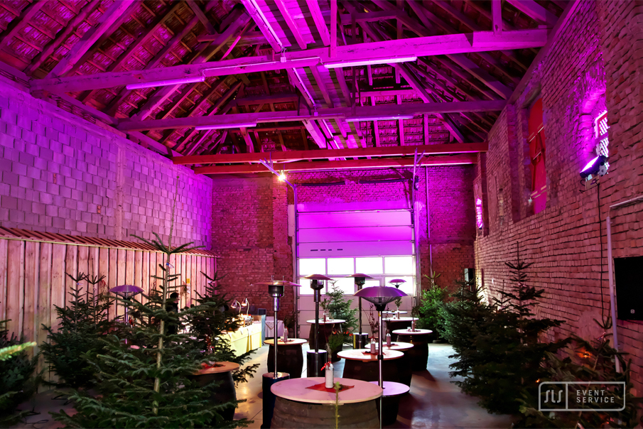 Weihnachtlich dekorierte Eventlocation mit Tannenbäumen, Stehtischen und pinker Beleuchtung