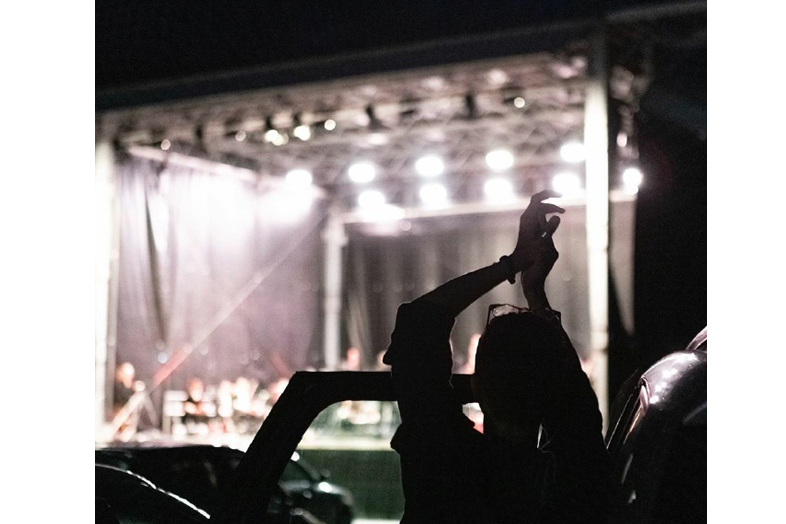 Silhouette einer Person neben einem Auto vor einer hell beleuchteten Open-Air-Bühne bei Nacht