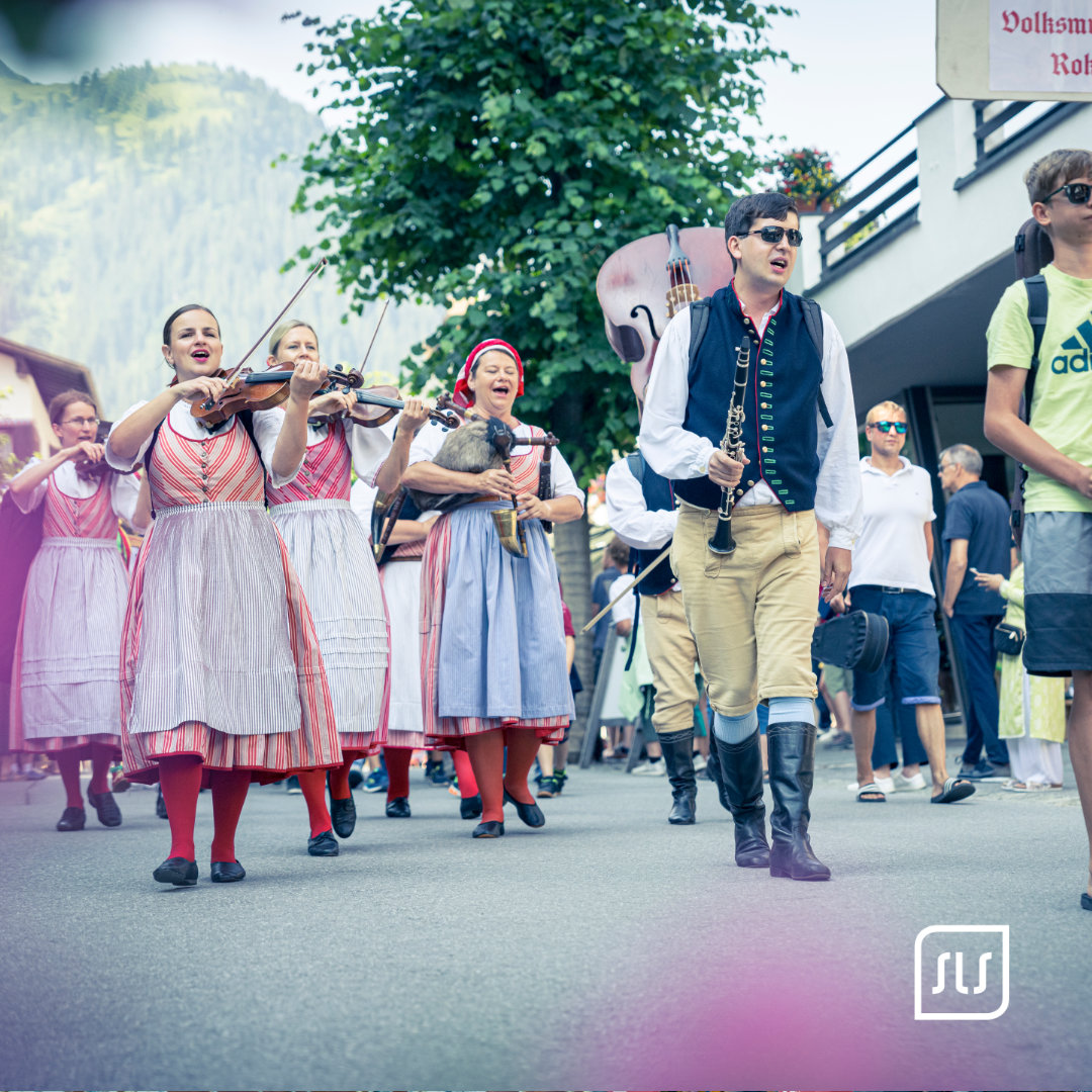 Musikgruppe in Tracht zieht mit Geigen und Blasinstrumenten durch St. Anton beim Dorffest 2023