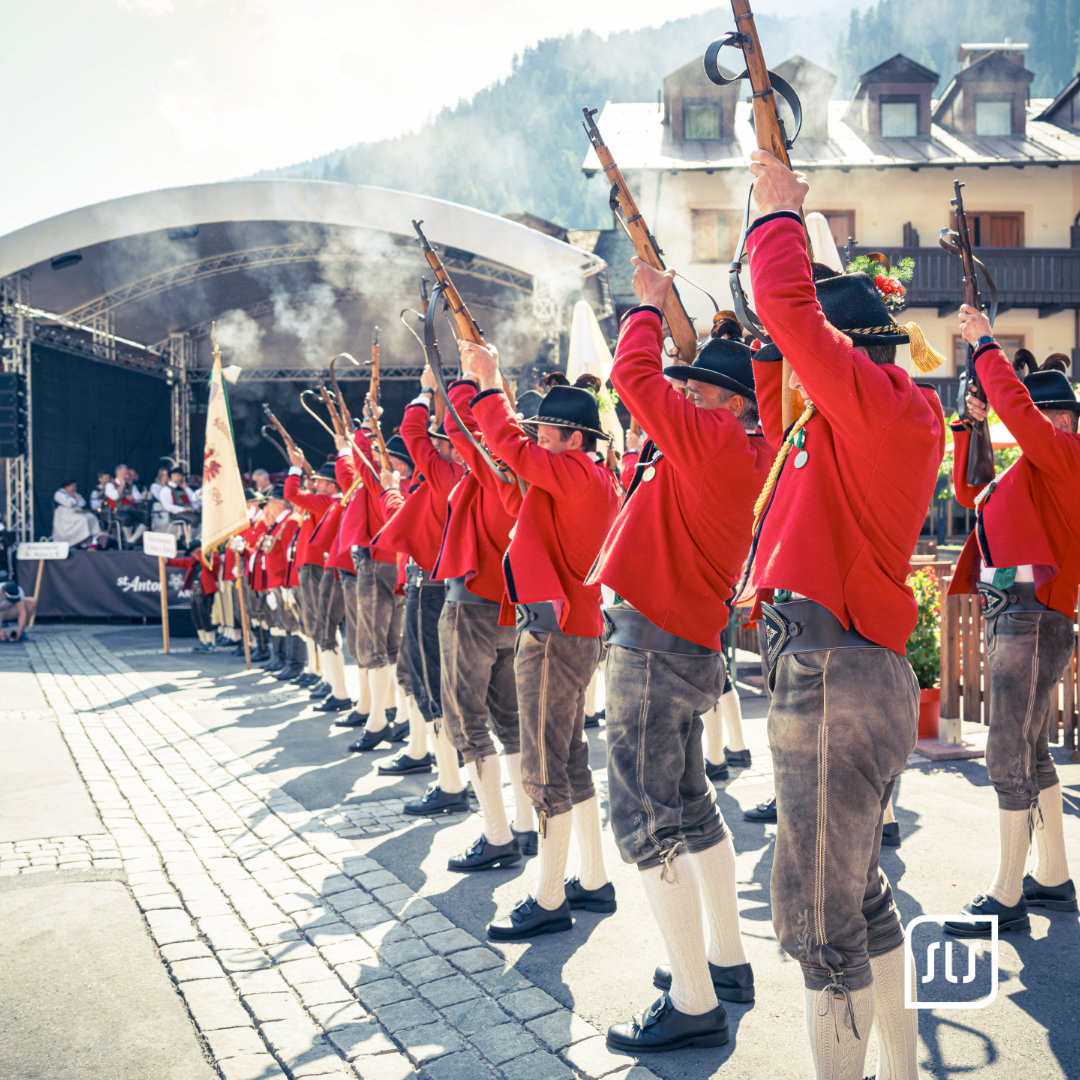 Traditionsgruppe in roten Jacken hebt beim Dorffest 2023 in St. Anton Gewehre vor der Bühne