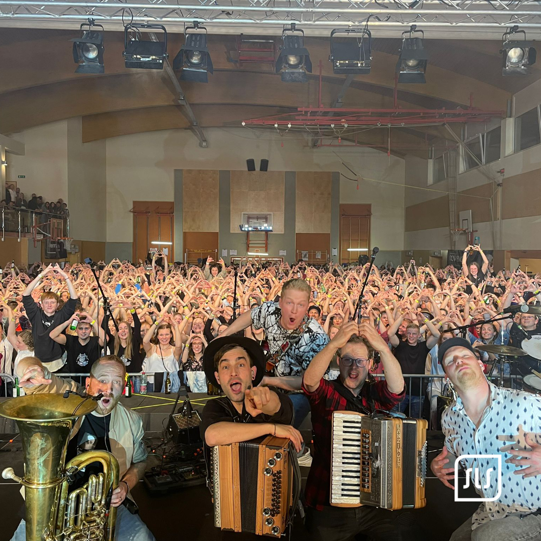 Fäaschtbänkler auf der Bühne mit Tuba und Akkordeons vor einem jubelnden Publikum in der Halle