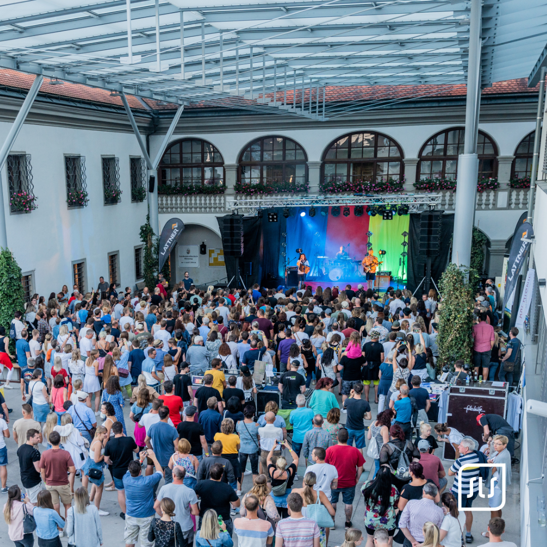 Viele Gäste verfolgen ein Konzert im überdachten Innenhof des Schlosscafés Sierning vor farbig beleuchteter Bühne