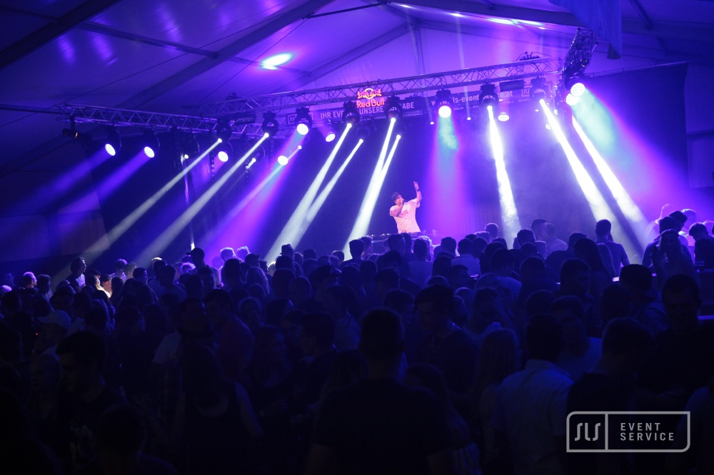 DJ auf einer Bühne vor großem Publikum mit blauer und violetter Lichtshow