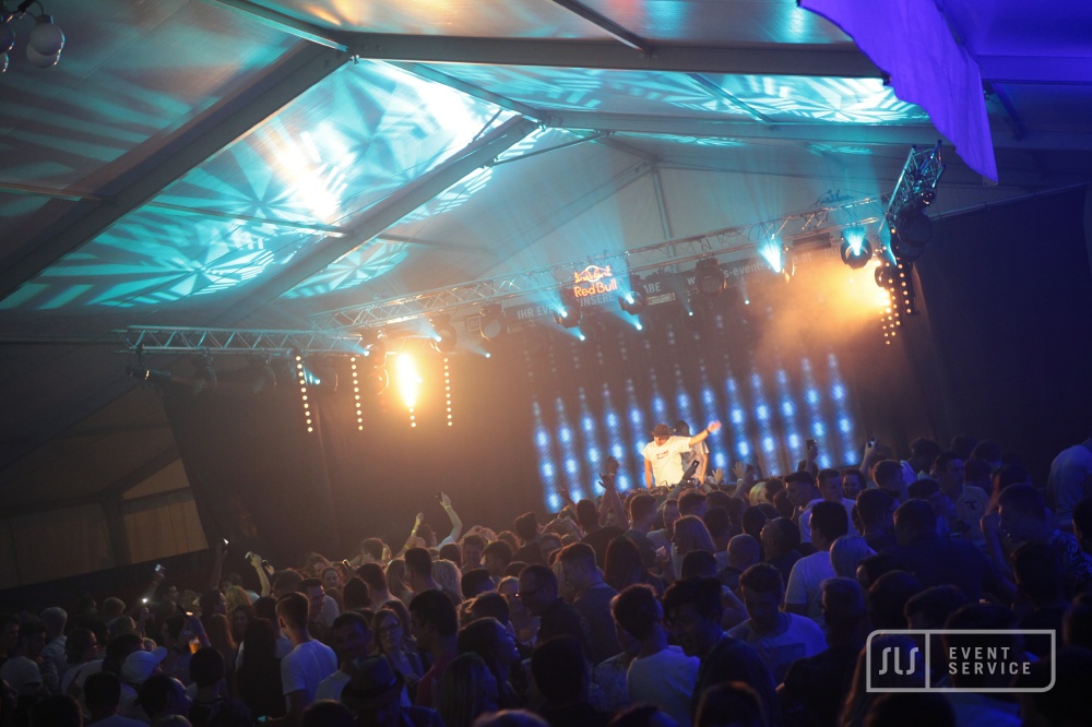 DJ auf einer Bühne vor großem Publikum mit türkiser und gelber Lichtshow