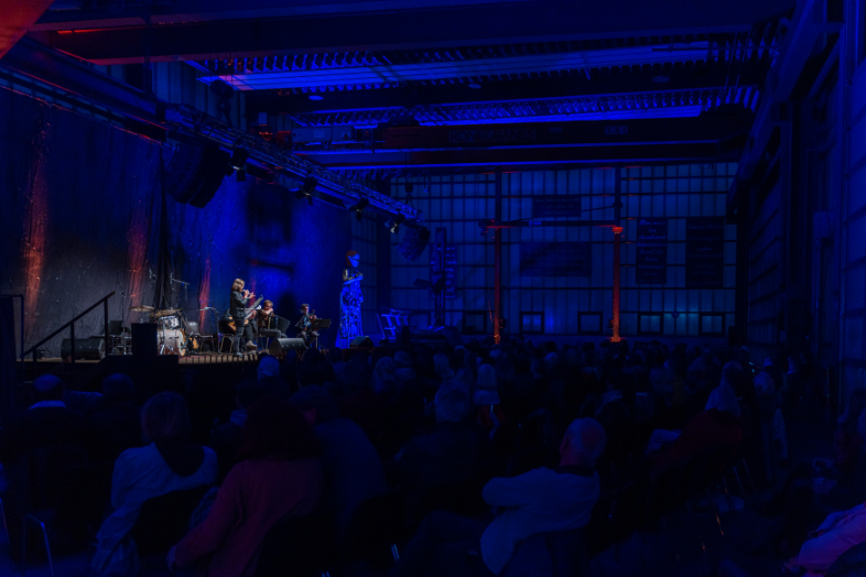 Publikum vor einer kleinen Bühne in blau beleuchteter Halle beim Literaturschiff in Mauterndorf