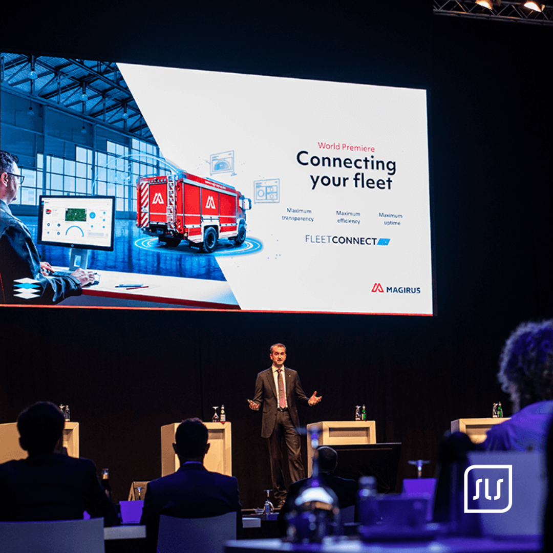 Redner vor einer Großbildfolie zu Magirus FleetConnect mit rotem Feuerwehrfahrzeug