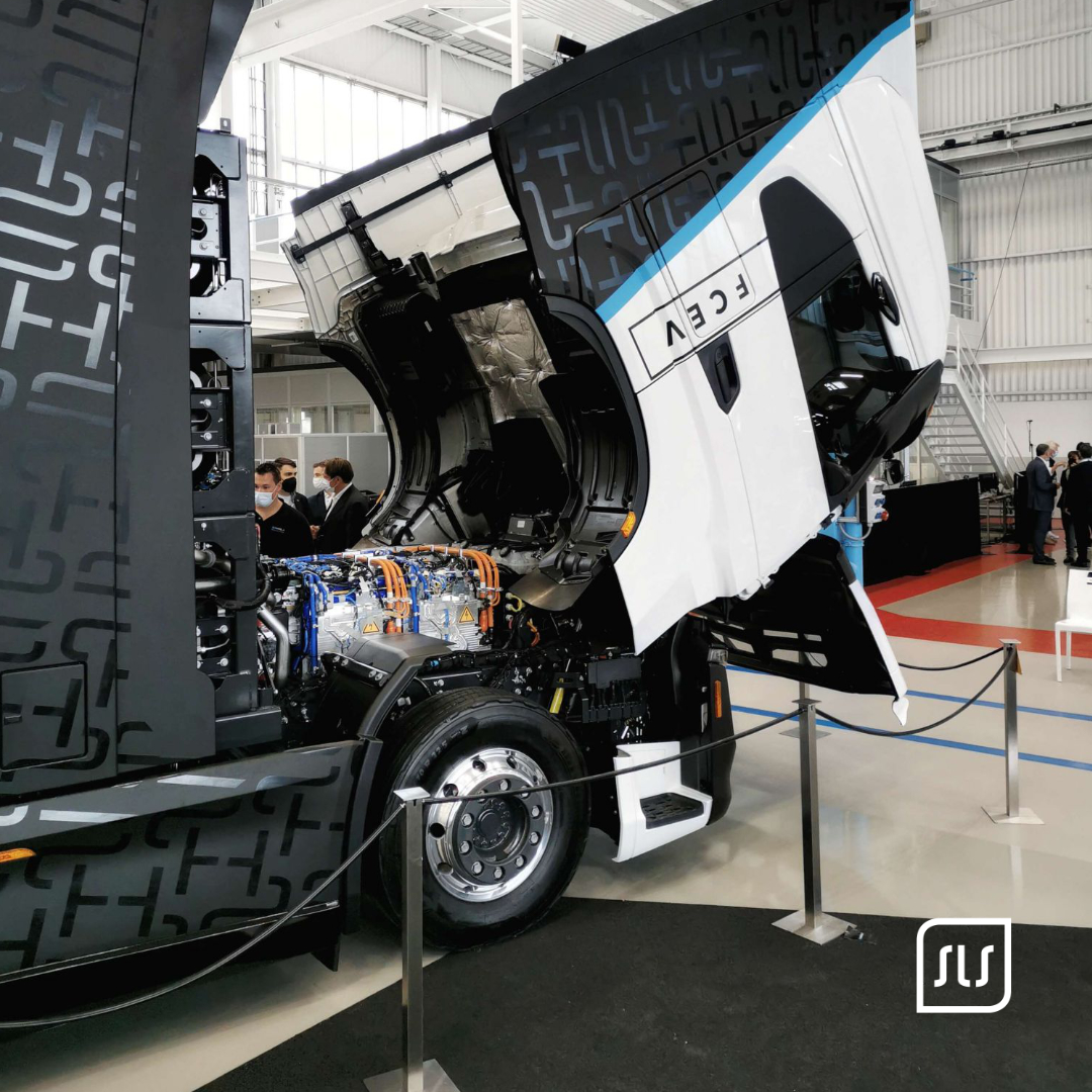 Weißer Nikola-Lkw mit gekippter Fahrerkabine und sichtbarer Fahrzeugtechnik in einer Ausstellungshalle