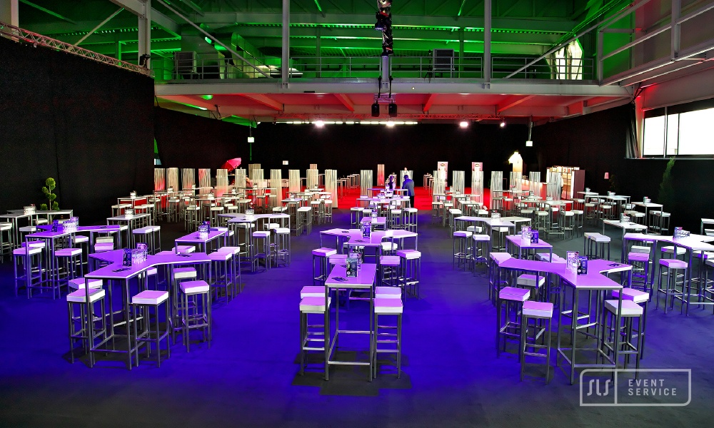 Vorbereitete Eventhalle mit zahlreichen Stehtischen, Barhockern und farbiger Beleuchtung