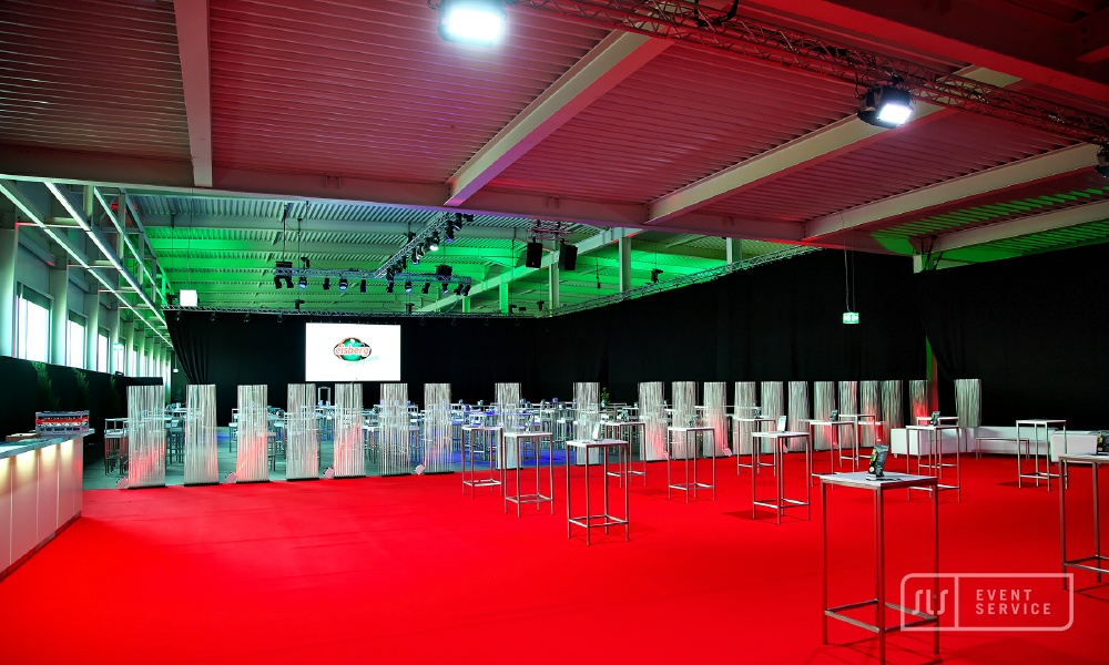 Modern ausgestattete Eventhalle mit rotem Teppich, Stehtischen und professioneller Lichttechnik