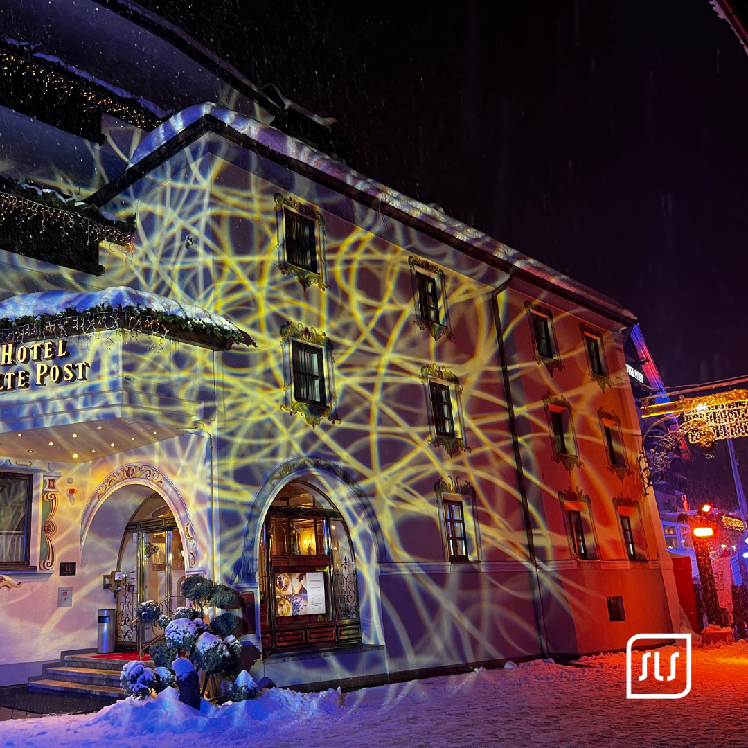 Abstrakte gelbe und blaue Lichtlinien werden nachts auf eine verschneite Hotelfassade in St. Anton projiziert