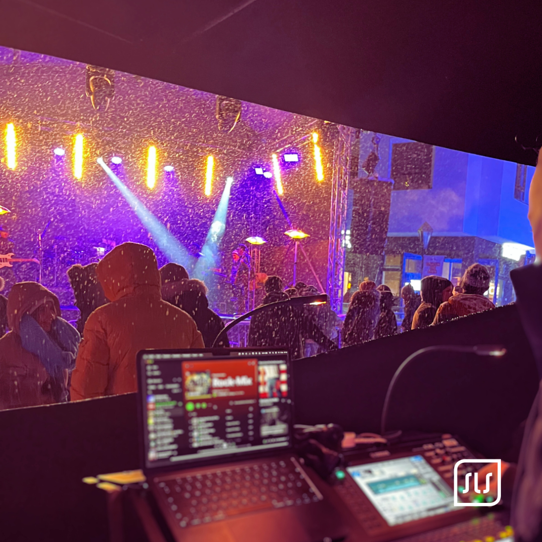 Laptop und Mischpult im Vordergrund, Publikum und beleuchtete Bühne im Schneefall beim Ski Open St. Anton 2023