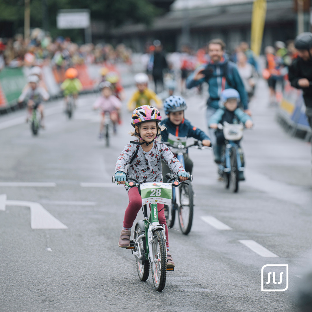 Kind mit Fahrradhelm fährt vor weiteren Kindern auf einer abgesperrten Straße in Dornbirn bei der Tour of Austria 2023