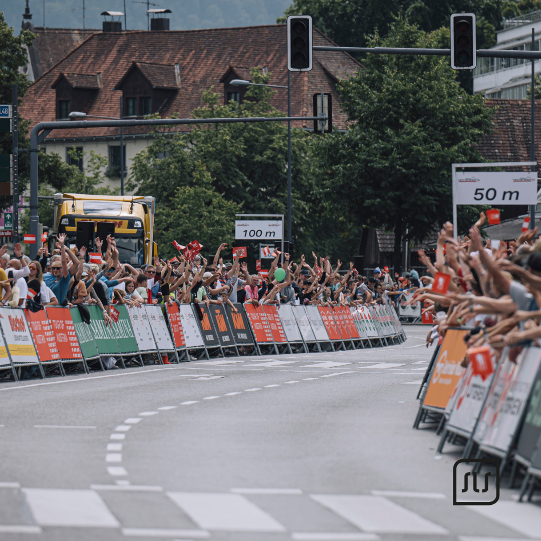 Zuschauer stehen hinter Absperrungen entlang der Zielgeraden der Tour of Austria 2023 in Dornbirn