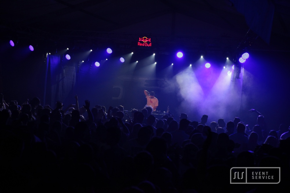 DJ auf einer Bühne vor großem Publikum mit blauer und violetter Lichtshow
