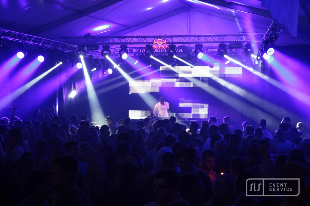 DJ auf einer Bühne vor großem Publikum mit blauer und violetter Lichtshow