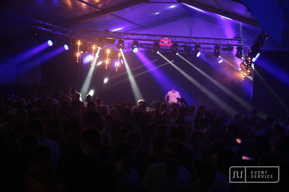 DJ auf einer Bühne vor großem Publikum mit violetter Lichtshow