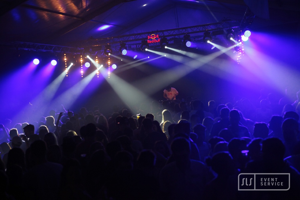 DJ auf einer Bühne vor großem Publikum mit blauer und violetter Lichtshow