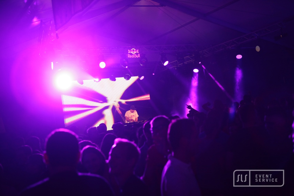 DJ auf einer Bühne vor großem Publikum mit pinkem und violetter Lichtshow
