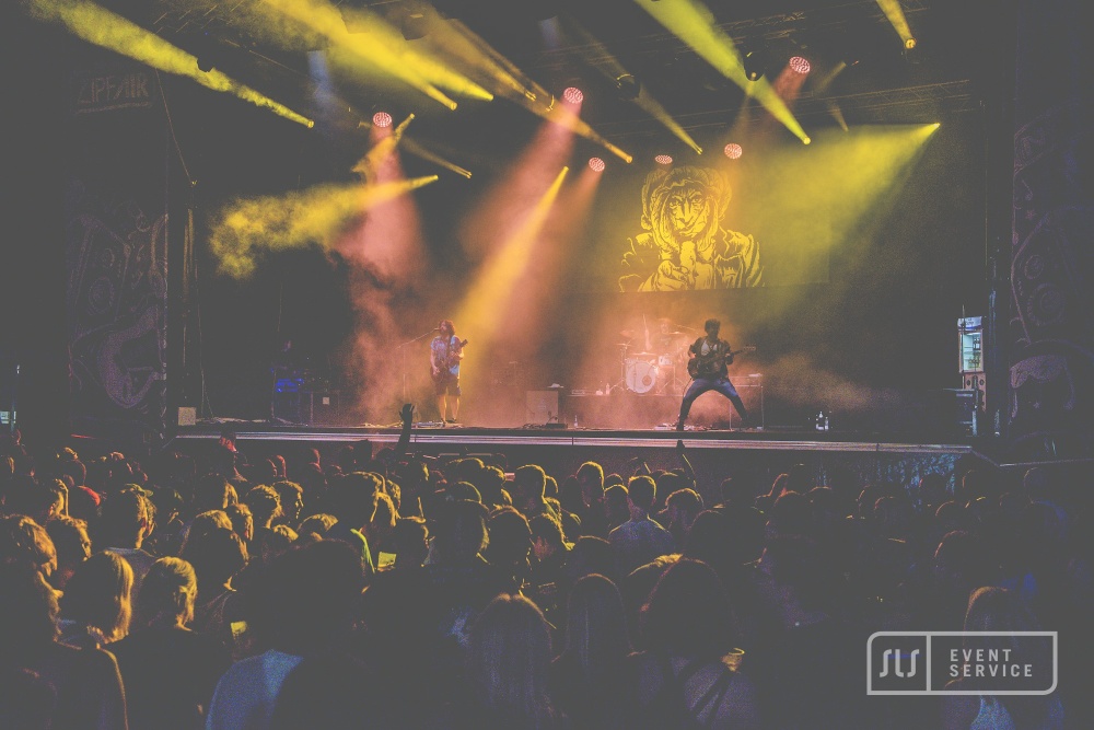 Live-Konzert mit Band, großem Publikum und gelber Bühnenbeleuchtung