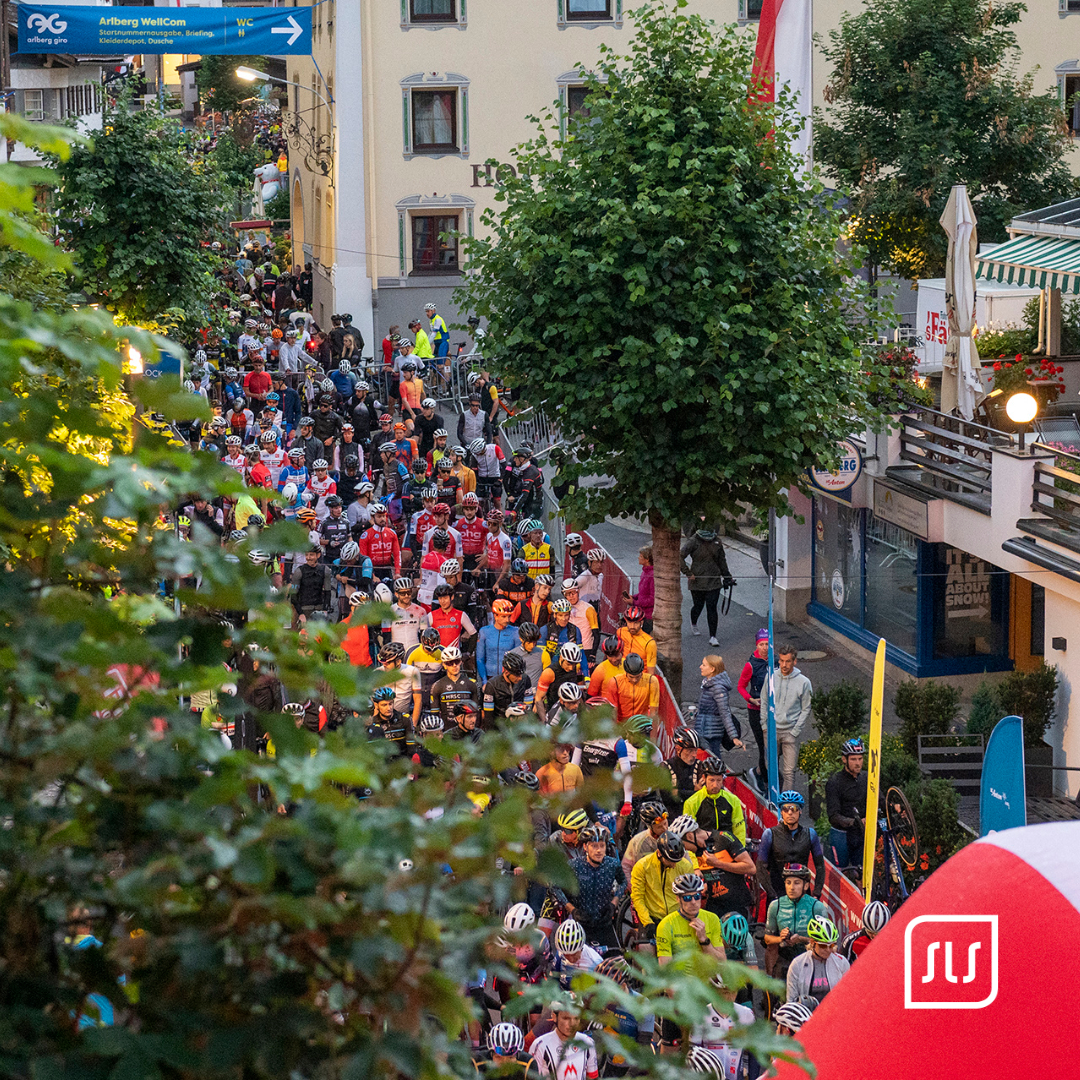 Großes Feld von Rennradfahrenden mit Helmen versammelt sich beim Start des Arlberg Giro 2022 in einer Ortsstraße