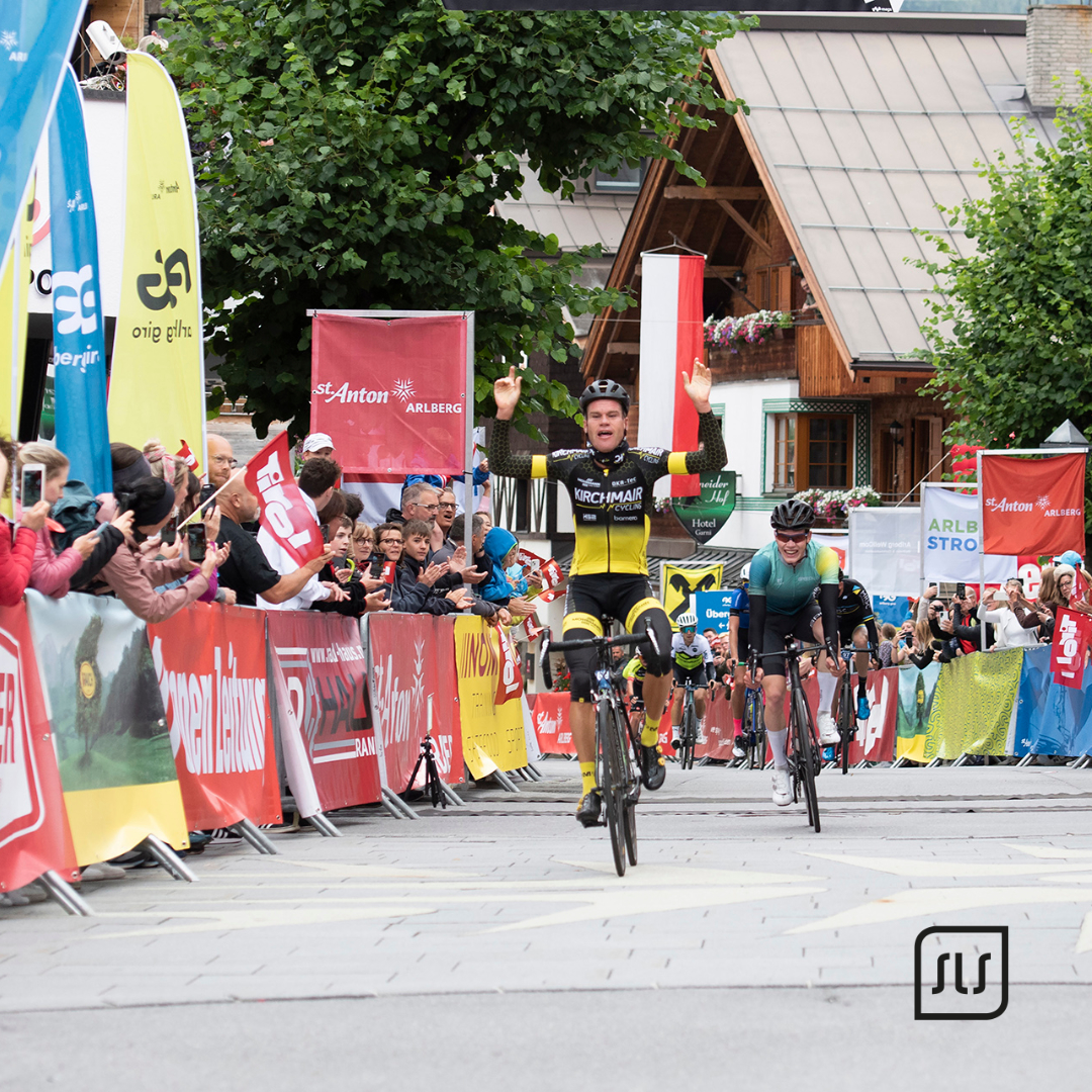 Radfahrer hebt im Zielbereich des Arlberg Giro 2022 beide Arme, während Zuschauer hinter Absperrungen applaudieren
