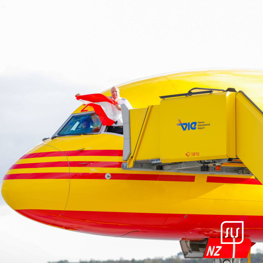 Person mit rot-weiß-roter Fahne an einem gelb-roten DHL-Flugzeug am Flughafen Wien