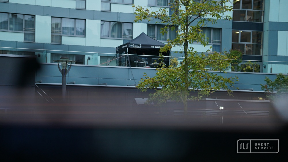 Schwarzes SLS-Eventservice-Zelt auf einer Terrasse vor einem Hotelgebäude
