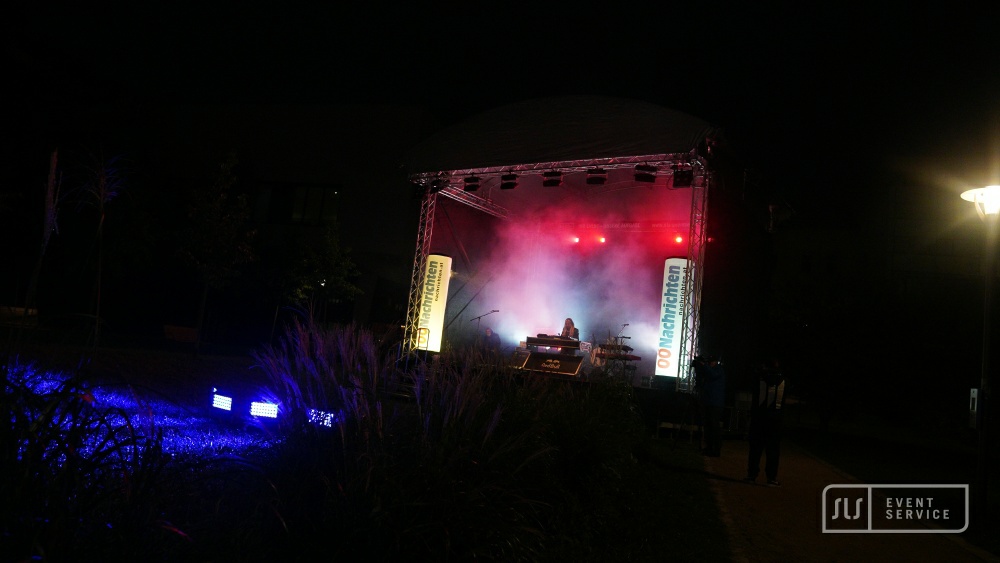 Open-Air-Bühne bei Nacht mit rotem Licht, Bühnennebel und einer Person hinter einem Pult