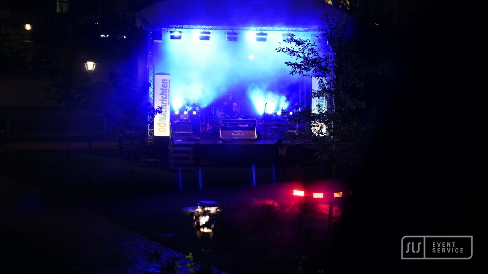 Open-Air-Bühne mit blauen Lichtstrahlen bei Nacht, vom dunklen Innenhof aus gesehen