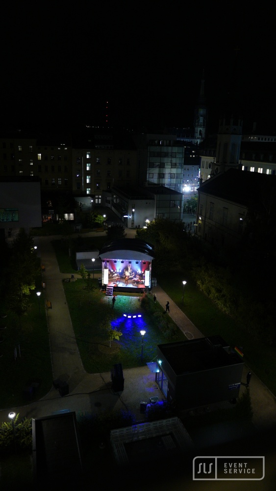 Blick von oben auf eine kleine beleuchtete Konzertbühne zwischen Gebäuden bei Nacht