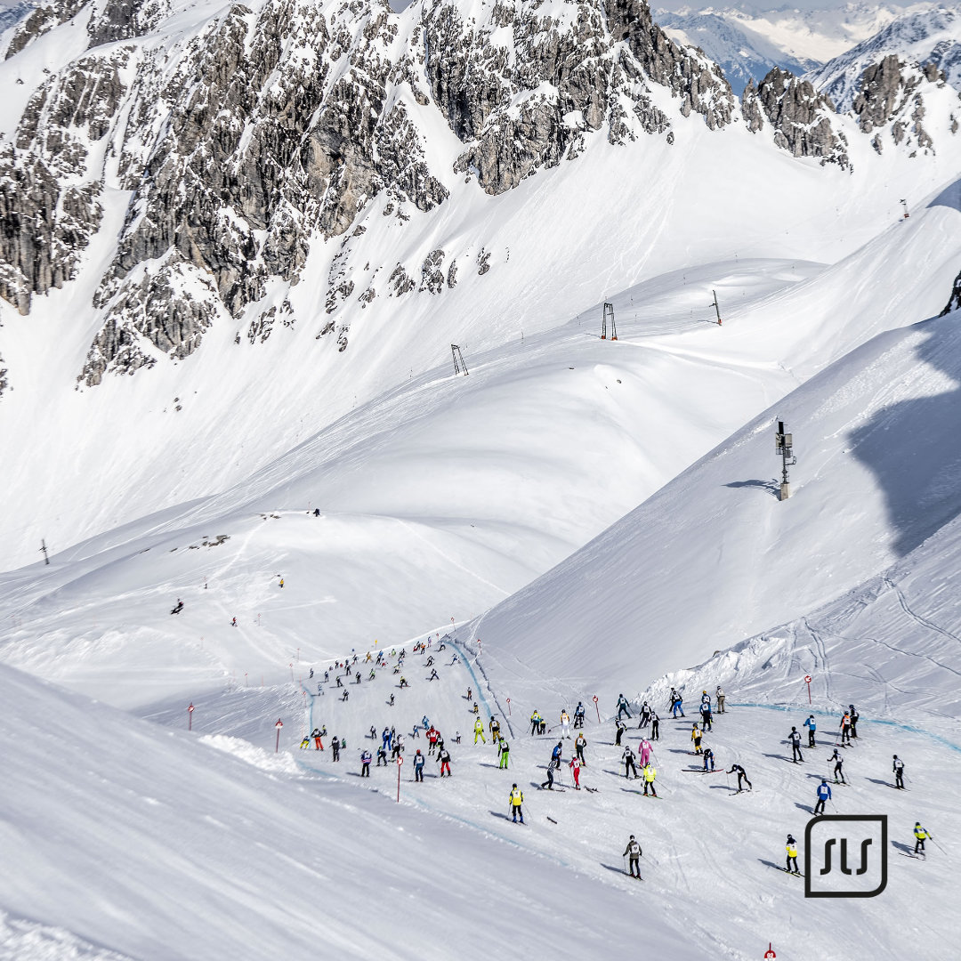 Viele Teilnehmende bewegen sich auf einer schneebedeckten Strecke zwischen steilen Gipfeln beim Event „Der weiße Rausch“ 2023