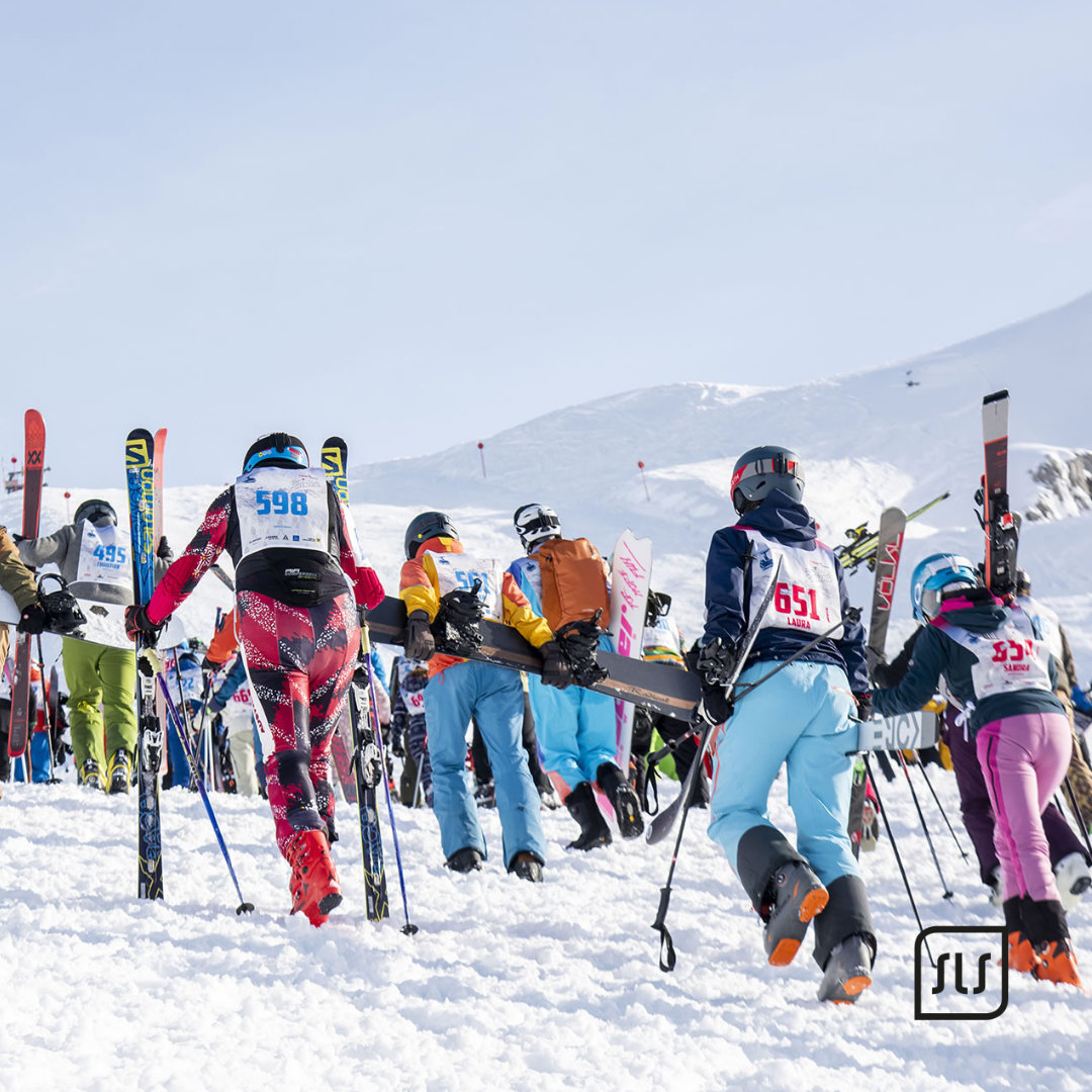 Teilnehmende mit Startnummern tragen ihre Ski durch den Schnee beim Event „Der weiße Rausch“ 2023