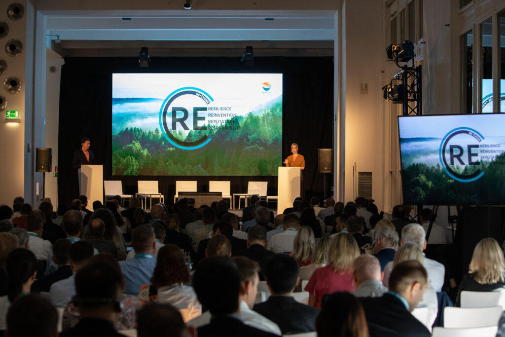 Zwei Vortragende an Rednerpulten vor einer großen Videowand bei PAPCON 2023; Publikum im Saal