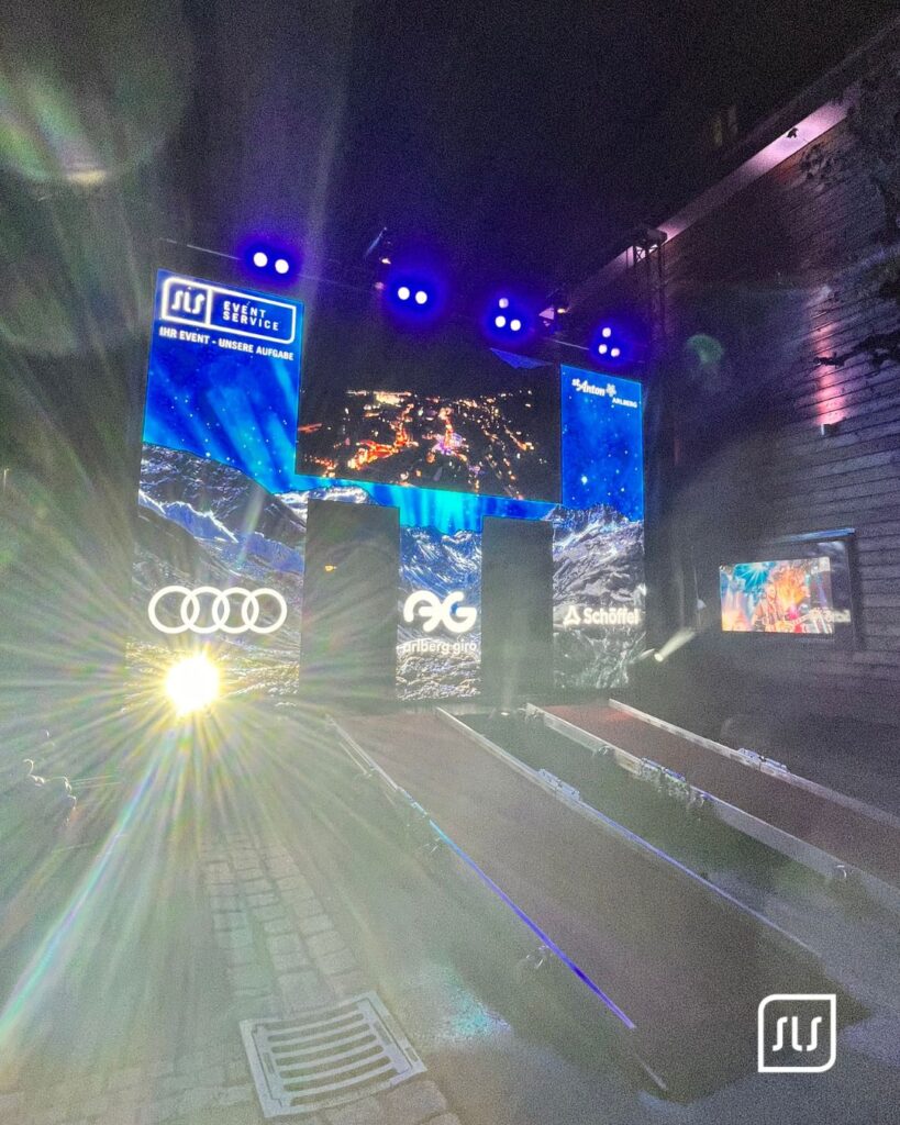 Blaue LED-Flächen und SLS Eventservice Branding beleuchten nachts den Eventbereich des Arlberg Giro 2026