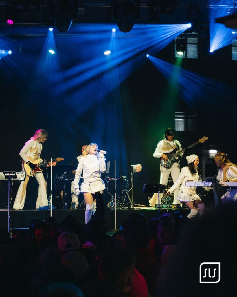 Sängerin mit Band in weißen Outfits auf blau beleuchteter Bühne beim Skiopen St. Anton 2025