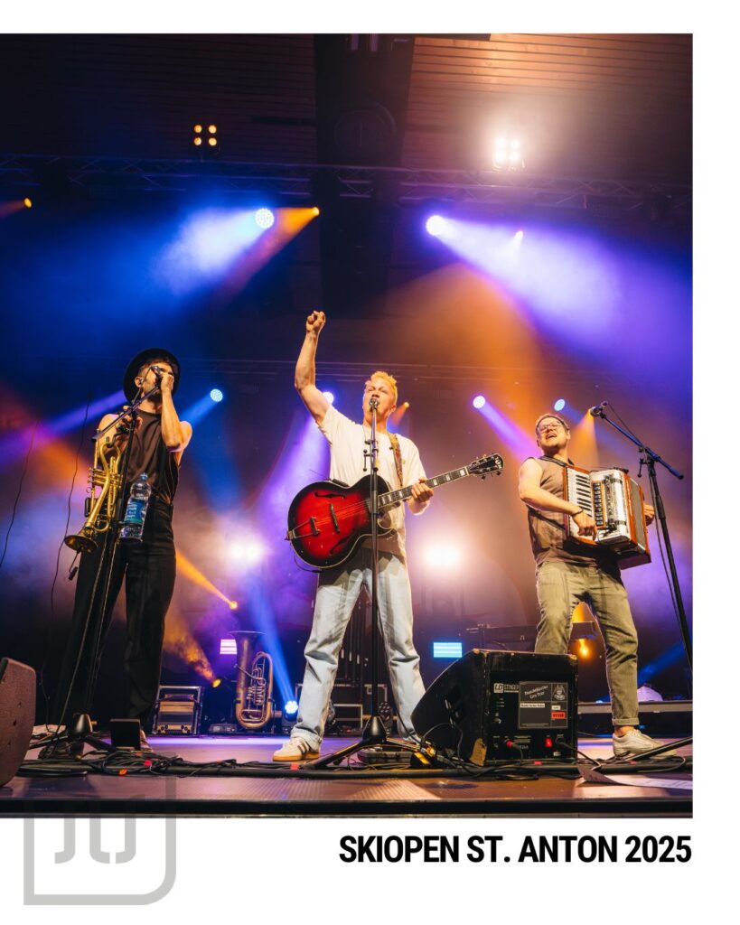 Drei Musiker mit Gitarre, Akkordeon und Blasinstrument auf der beleuchteten Bühne beim Skiopen St. Anton 2025