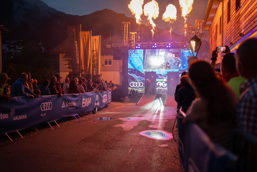 Nächtlicher Zielbereich des Arlberg Giro 2026 mit Flammeneffekten, LED-Wand und Publikum